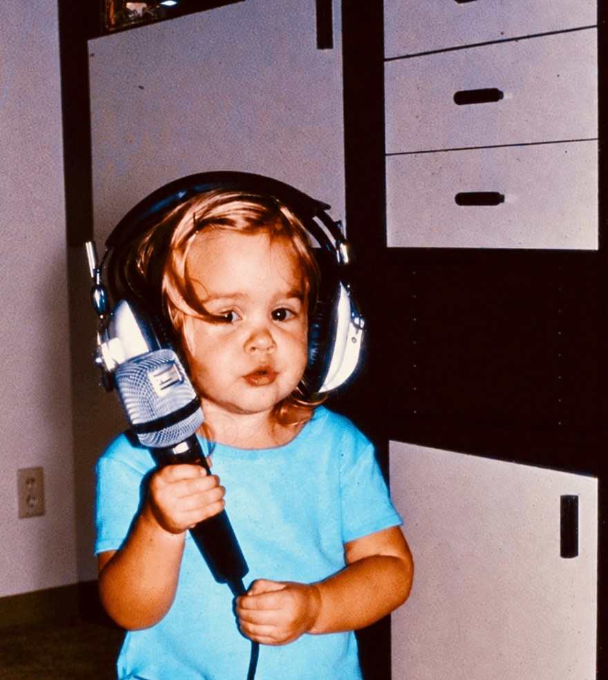 Mirell as a child wearing headphones and holding a microphone.